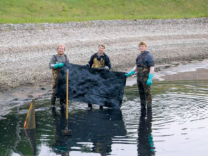 Steve Koski (L) and Austin Dusek (R), both with the Minnesota DNR, and Prof. Tim Stark (center), University of Illinois, holding one of the geomembrane samples cut from the longer sample that still remains on the bottom of the sedimentation basin under 6 inches of sand cover. This sample was delivered to the UIUC labs for testing. 