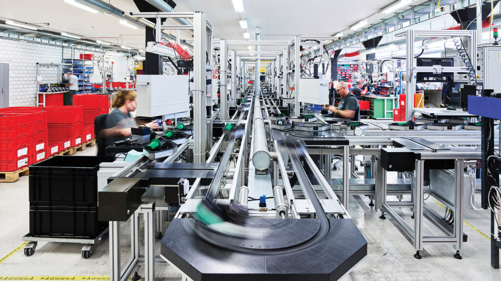 A factory floor showing production of Leister hand tools. The conveyer is shown as a blur.