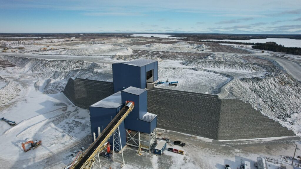 Aerial view of a large, structured earthworks site with a tall geosynthetic reinforced wall, snowy landscape, and machinery.