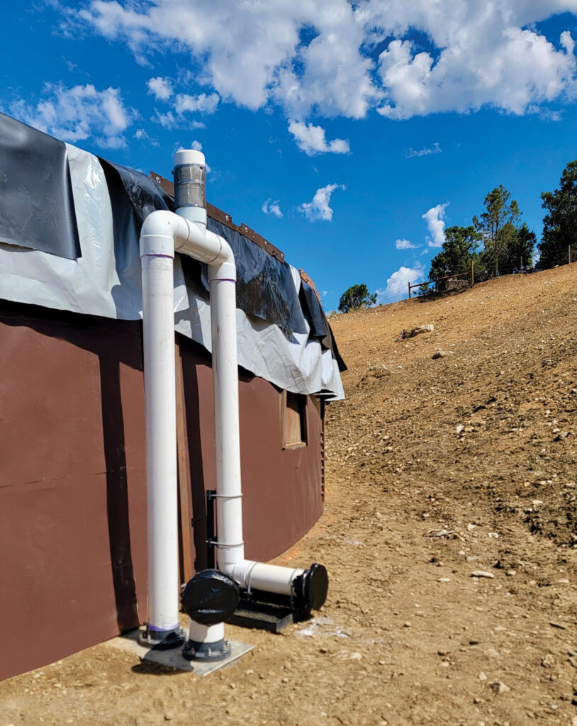 A temporary water tank with white piping and a black pump, set against a brown earth hillside and blue sky with scattered clouds.