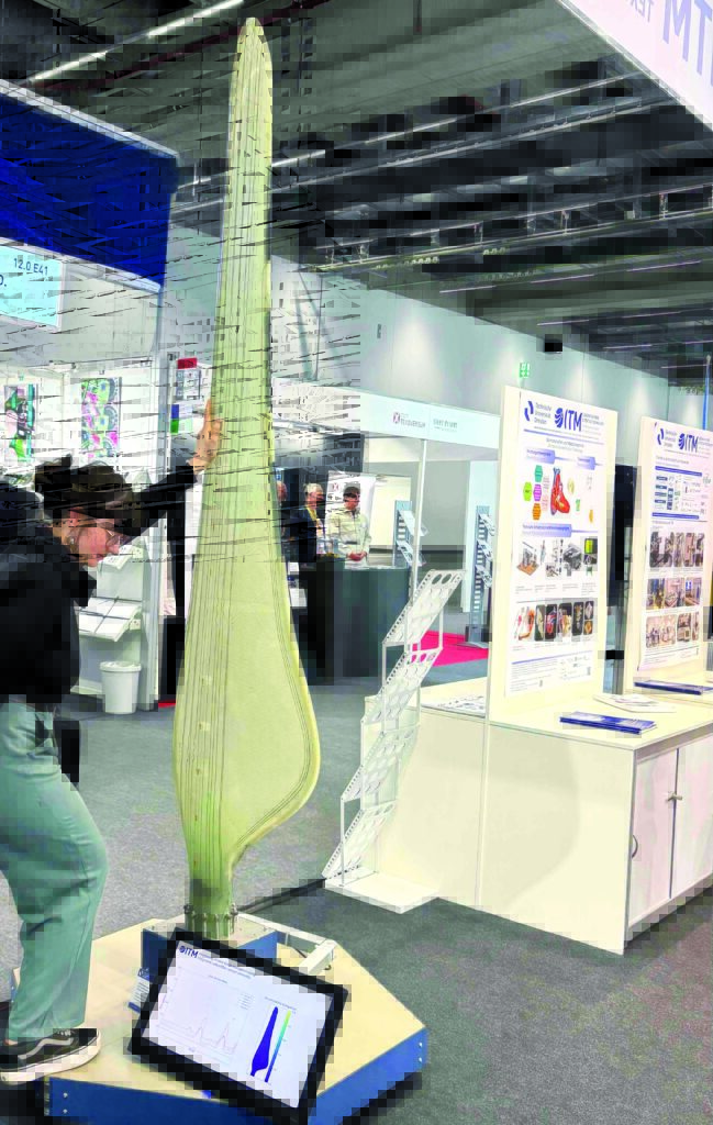 A person interacts with a large, blade-like structure on a display stand, surrounded by a modern exhibition setting with posters.